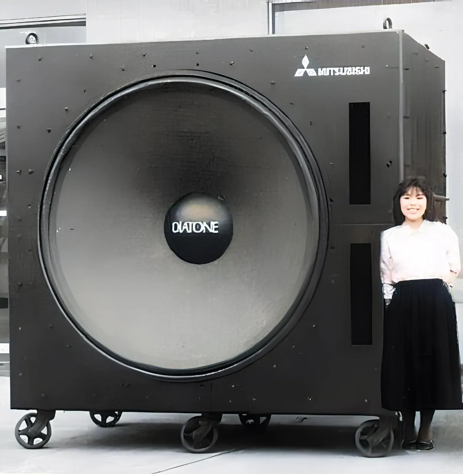 A HUGE subwooder with a woman standing next to it. She looks tiny in comparison. The woofer is the Diatone, by Mitsubishi, capable of producing minor earthquakes.