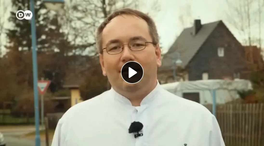 A sharp looking dyne standing in front of a camera in a white doctor jacket.