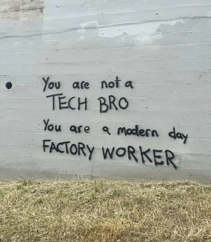 Graffiti on the wall: "you are not a TECH BRO you are a modern FACTORY WORKER"